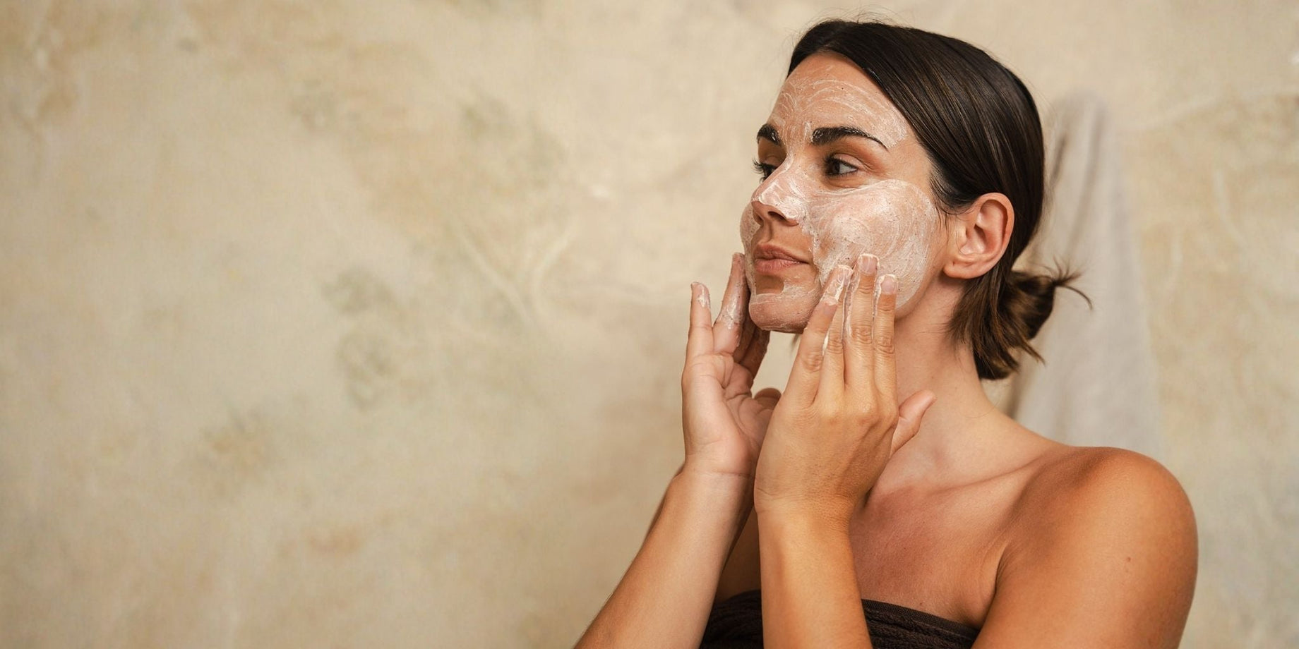 Woman applying a creamy facial mask as part of a Certified Organic skincare routine.