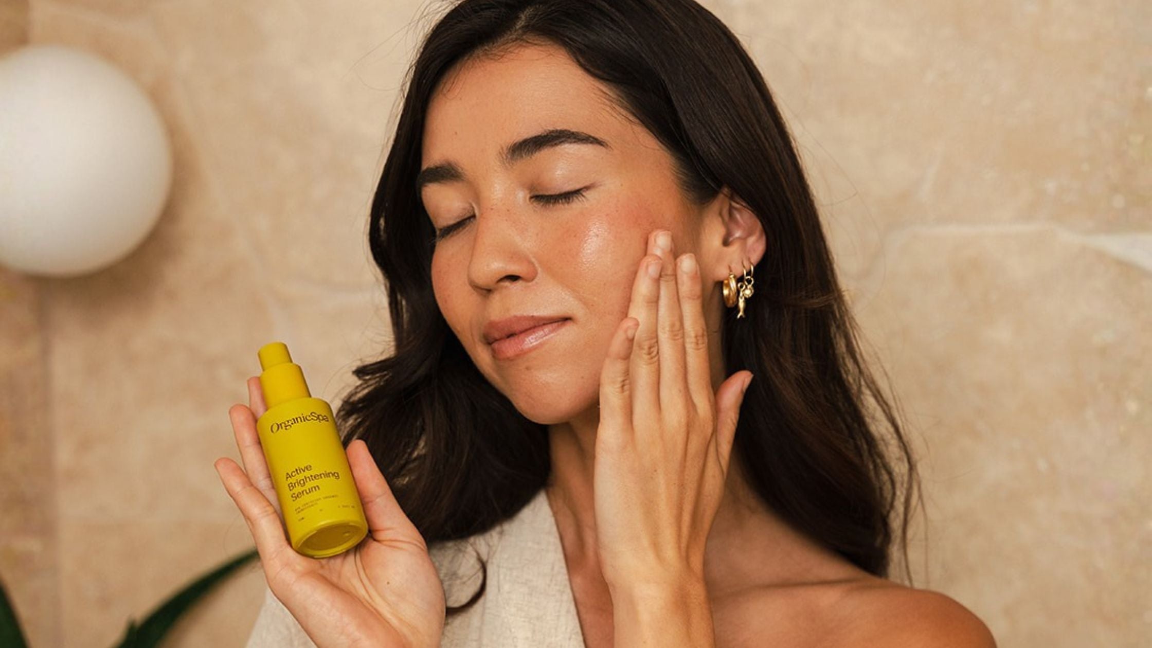 Woman with radiant skin holding OrganicSpa Active Brightening Serum, a certified organic vitamin C serum