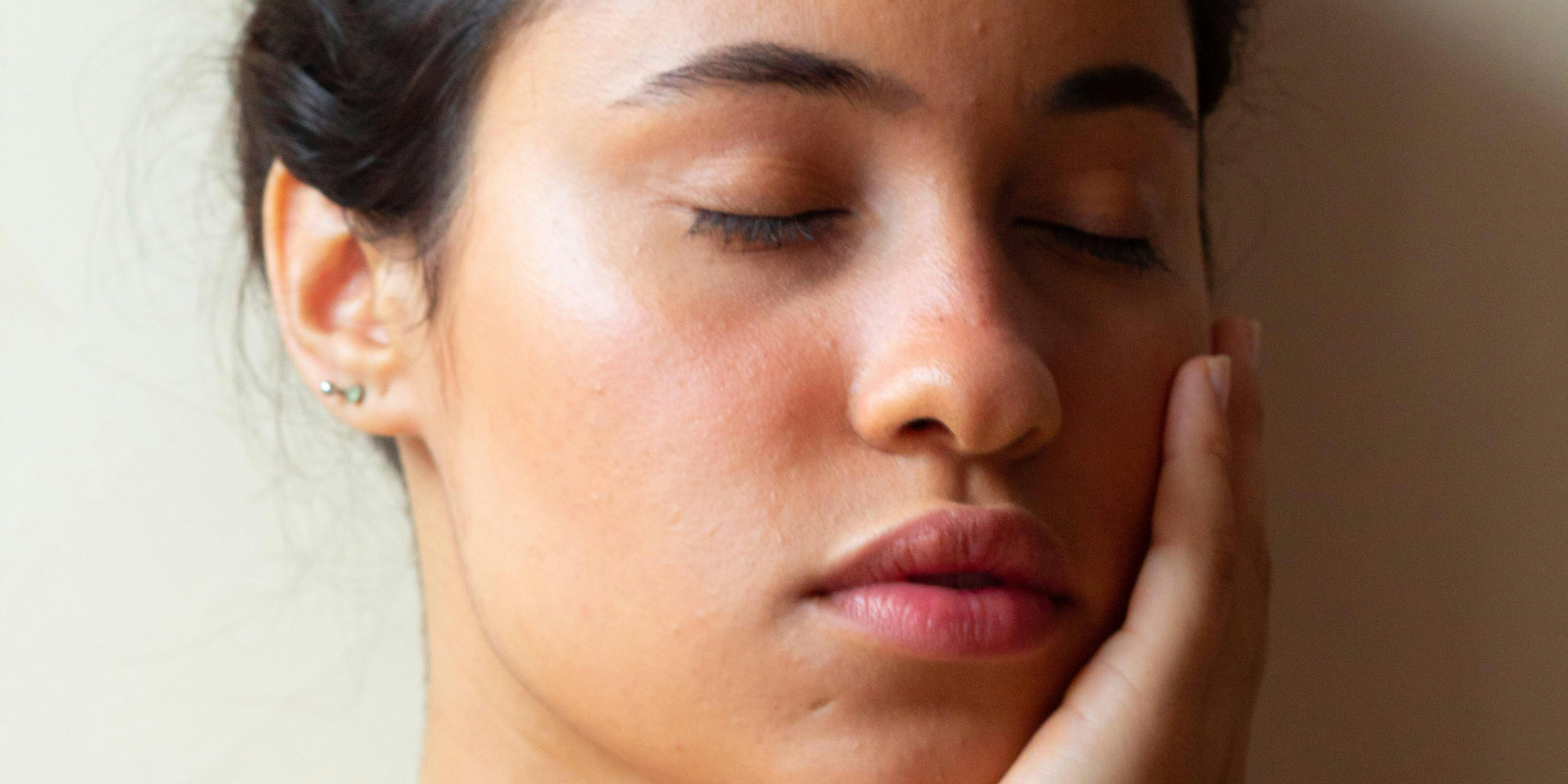 Woman with eyes closed gently touching her face, showing sensitive skin with mild redness.