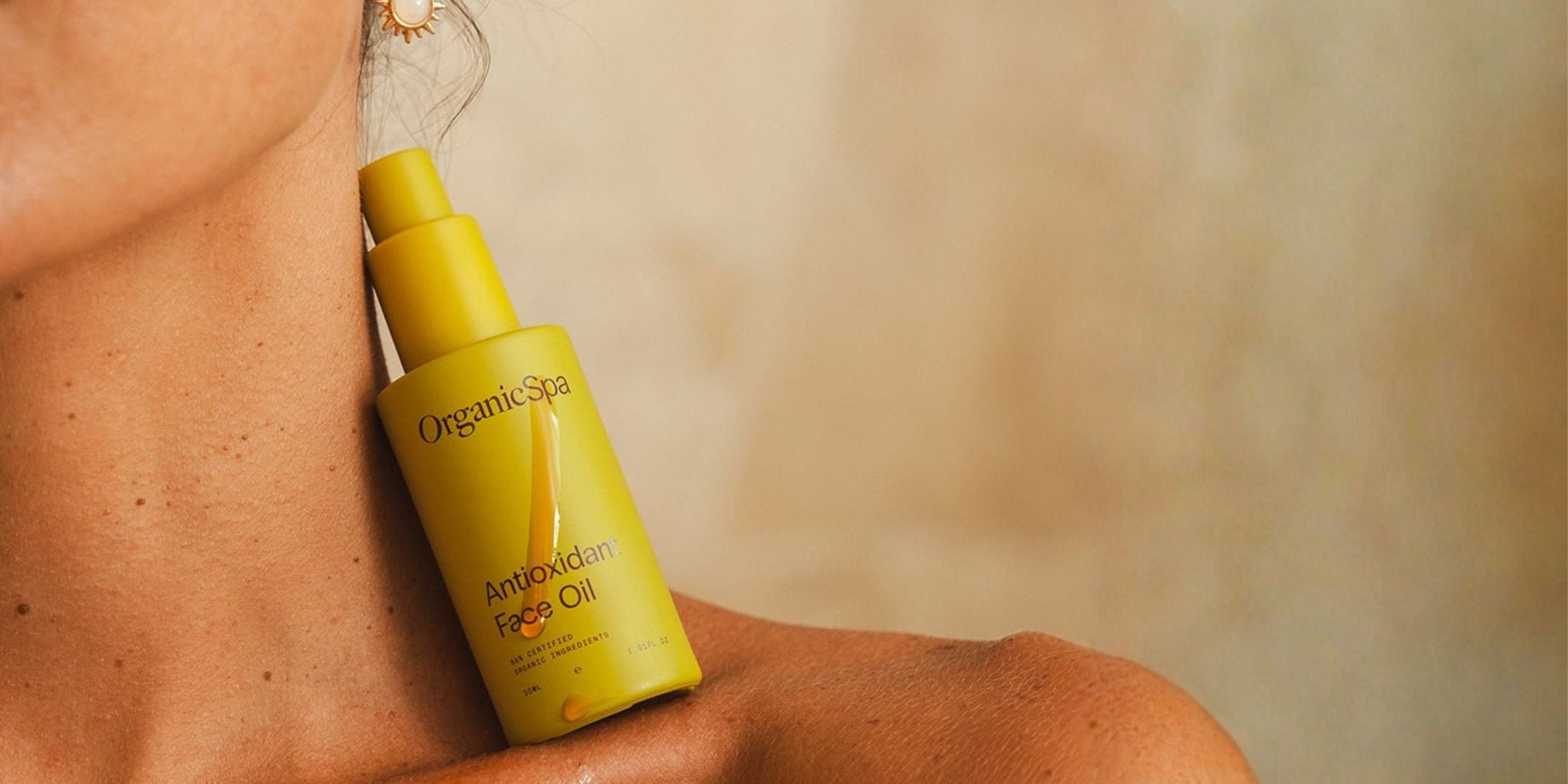Close-up of a woman’s shoulder and neck with Organicspa Antioxidant Face Oil bottle resting against her skin.