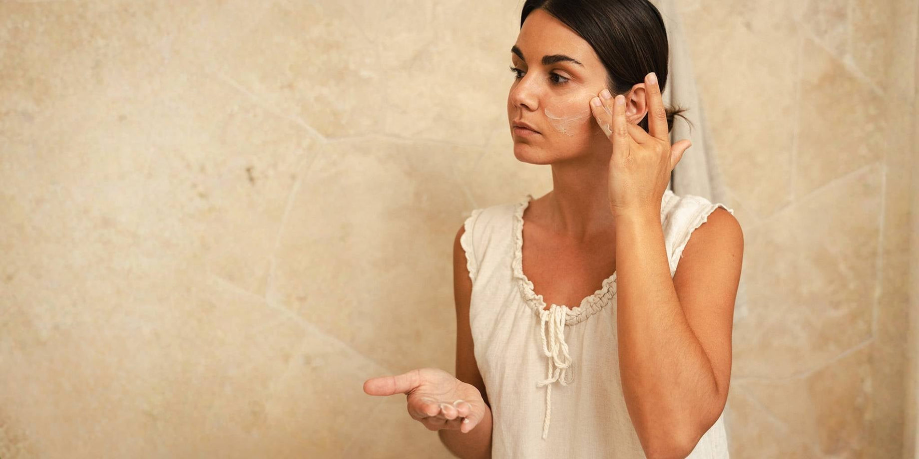 Woman applying moisturiser in a bathroom, representing Organic Spa’s Certified Organic skincare routine for tone, texture and radiance.