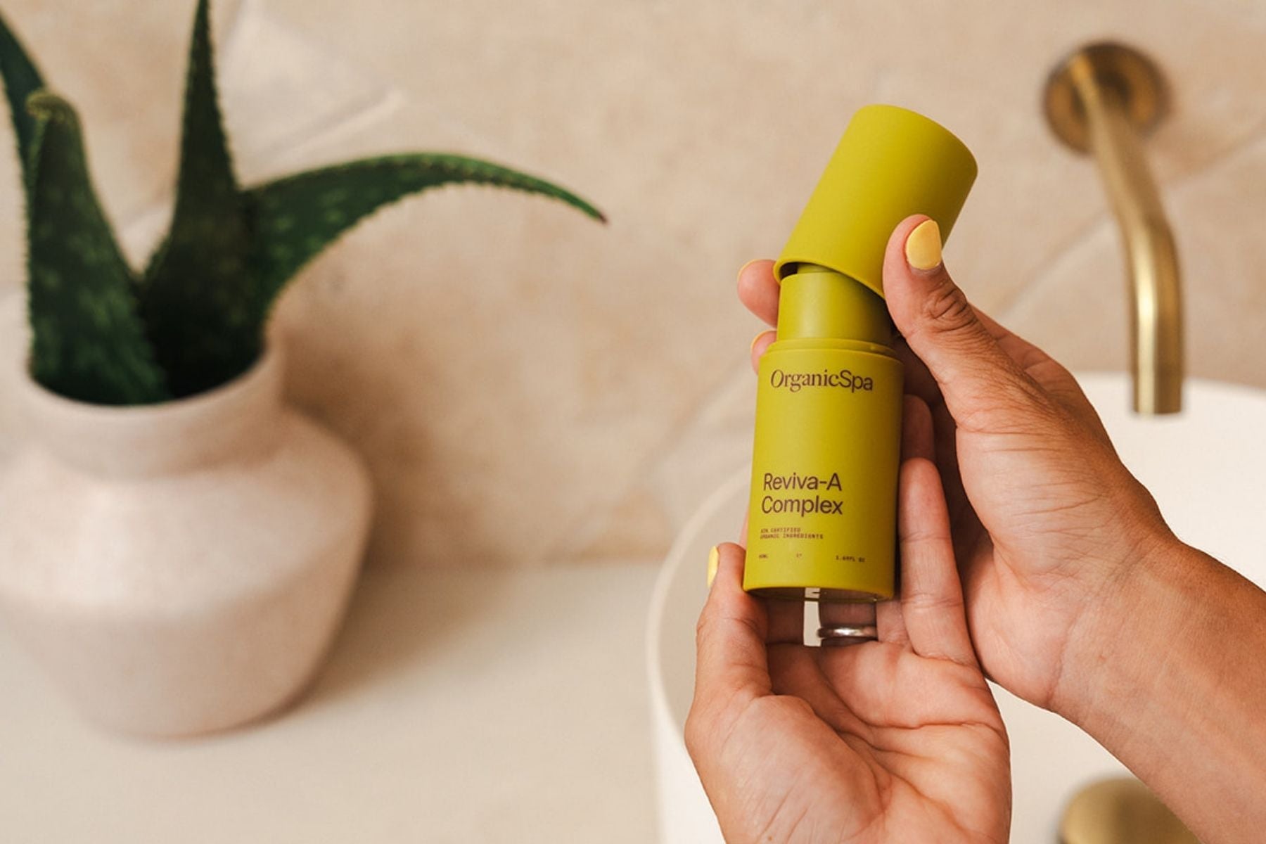Hands holding Organic Spa Reviva-A Complex in a warm bathroom setting