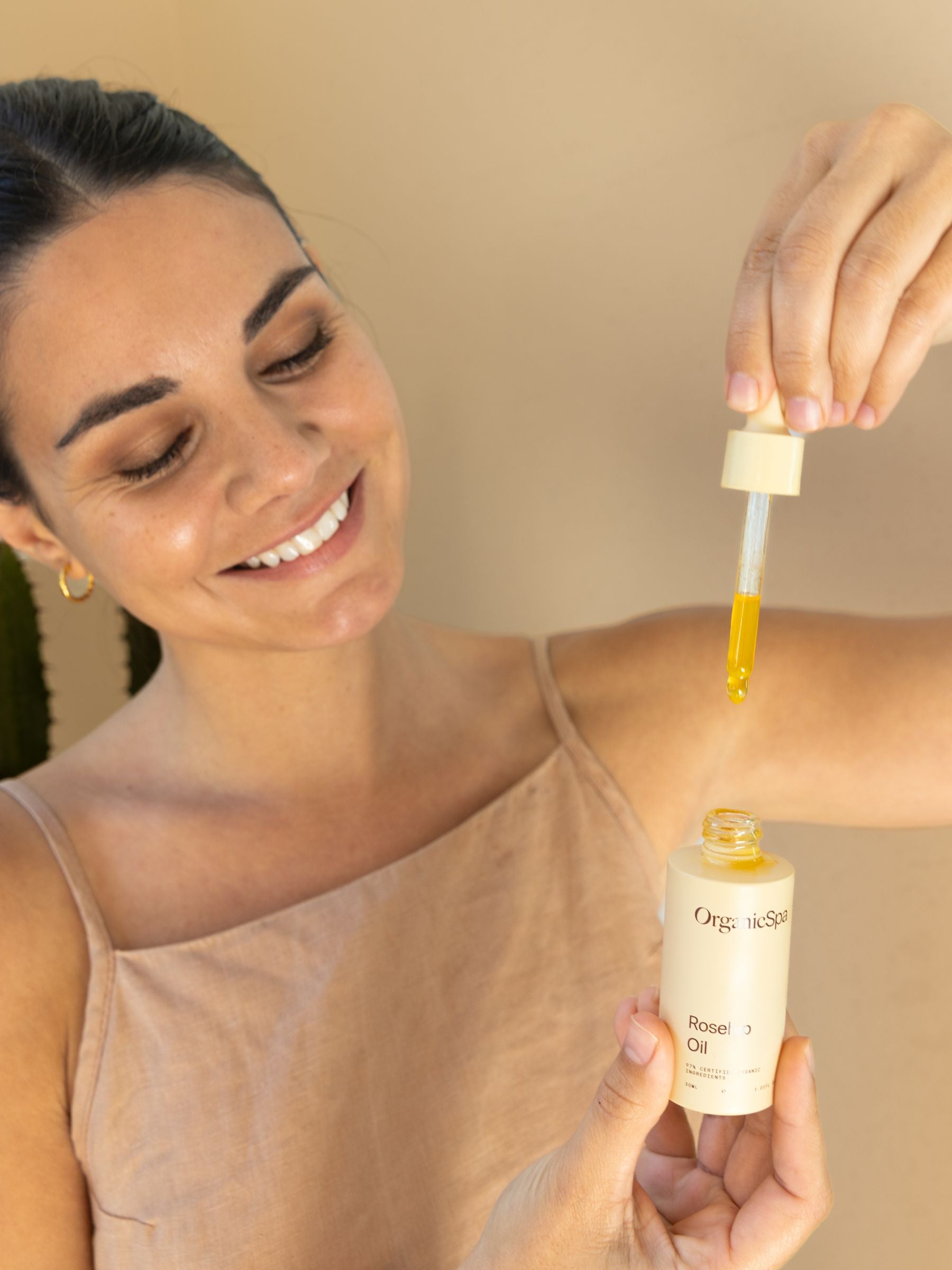 Dark haired woman holding OrganicSpa rosehip oil in glass dropper - Australian Made