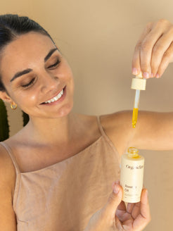 Dark haired woman holding OrganicSpa rosehip oil in glass dropper - Australian Made