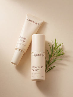 OrganicSpa Blemish Control and Vitamin C Serum laid flat on a warm cream background, styled with a fresh sprig of tea tree — a nod to the certified organic botanicals within. Certified Organic Skincare.