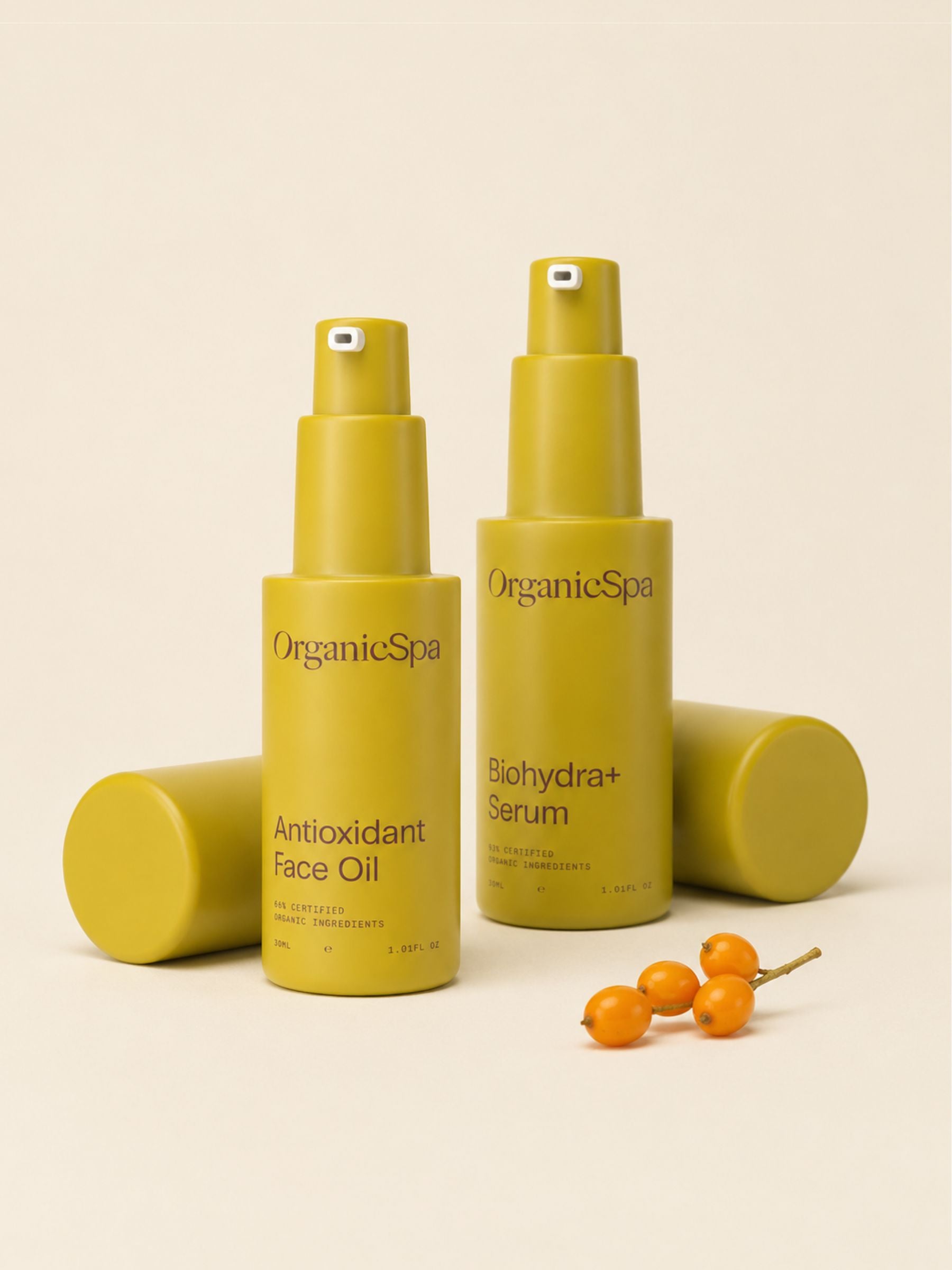 OrganicSpa Antioxidant Face Oil and Biohydra+ Serum on a warm cream background, styled with a small cluster of sea buckthorn berries — a nod to the antioxidant-rich organic botanicals within. Certified Organic Skincare.