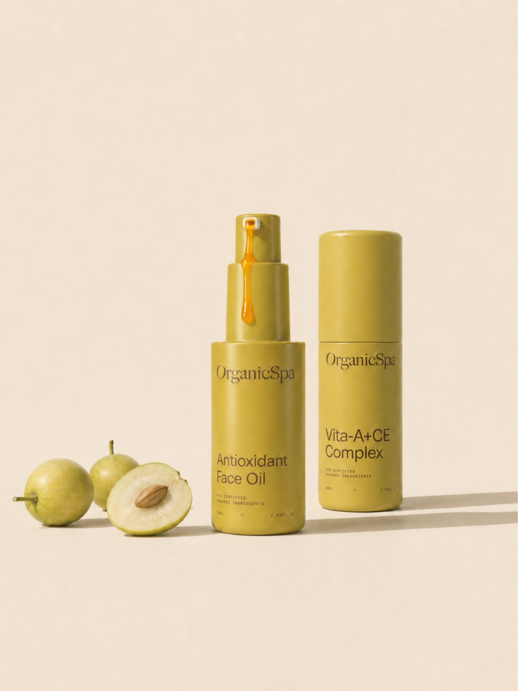 OrganicSpa Antioxidant Face Oil and Vita-A+CE Complex on a warm cream background, styled with fresh marula fruit — a rich source of antioxidants and the hero ingredient in the face oil. A drop of amber oil is visible on the pump. Certified Organic Skincare.