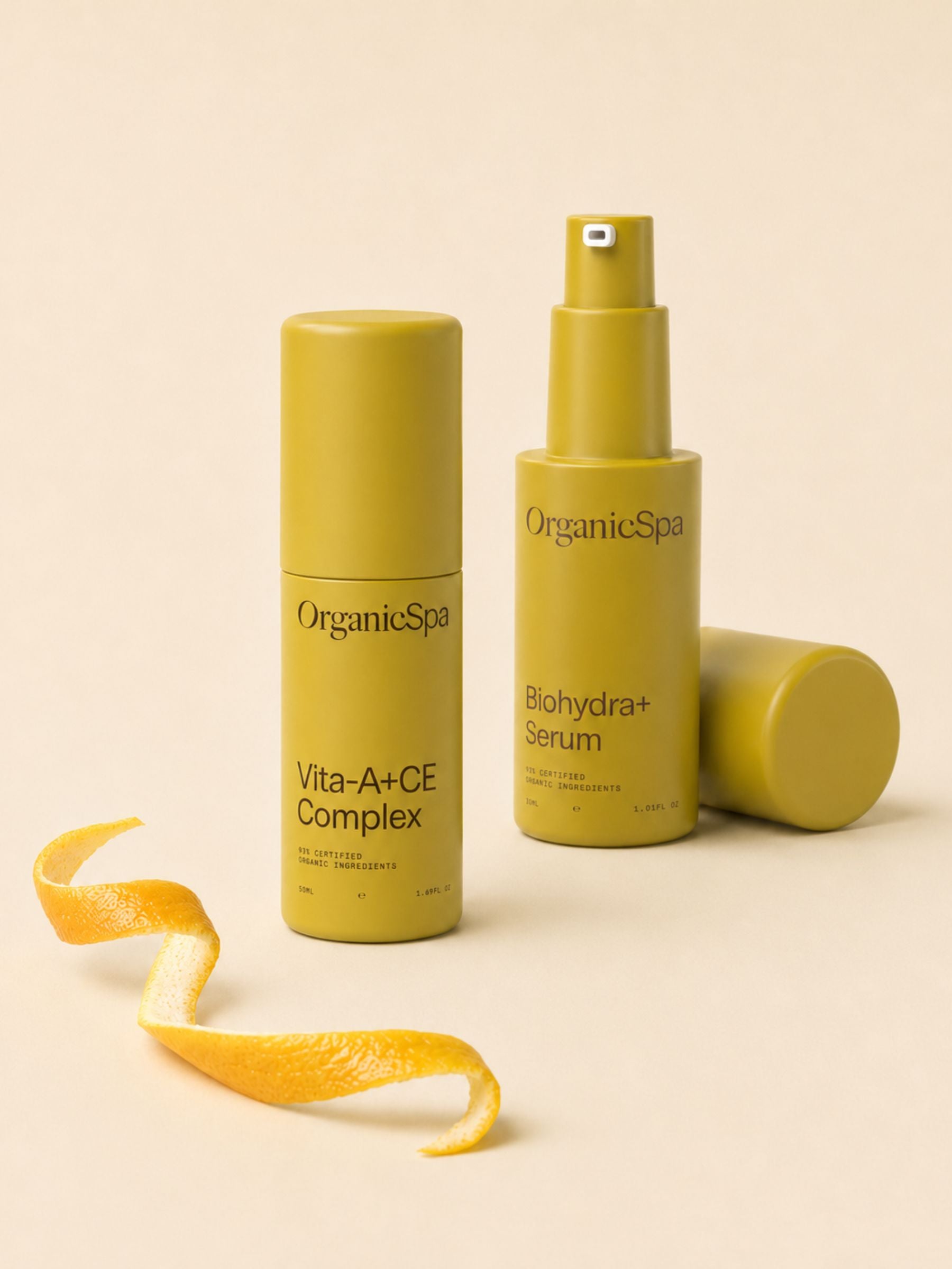 OrganicSpa Vita-A+CE Complex and Biohydra+ Serum on a warm cream background, styled with a curled citrus peel - a nod to the vitamin-rich organic ingredients within. Certified Organic Skincare.
