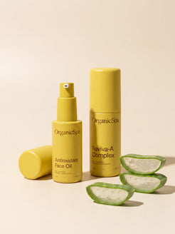 OrganicSpa Antioxidant Face Oil and Reviva-A Complex on a warm cream background, styled with freshly cut aloe vera — reflecting the soothing, skin-repairing organic botanicals within. Certified Organic Skincare.