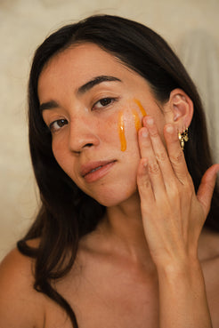 Woman applying a golden Organic Spa facial serum or oil to her cheek, highlighting the luminous texture on the skin.