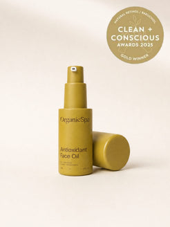 OrganicSpa Biohydra+ Serum, a chartreuse bottle held upright in one hand against a pale background. Two badges beside it: Organic Beauty winner 2026, and Silver winner in the Serum category at the Clean + Conscious Awards 2025.