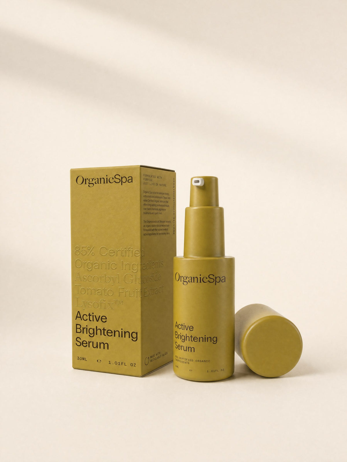 OrganicSpa Active Brightening Serum, a chartreuse 30ml bottle with its cap off, standing beside its matching carton. The carton reads 85% Certified Organic Ingredients, Ascorbyl Glucoside, Tomato Fruit Extract, Lysofix, and made with recyclable glass.