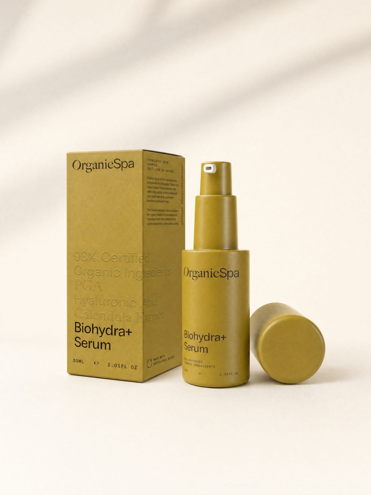 OrganicSpa Biohydra+ Serum, a chartreuse 30ml pump bottle with its cap lying beside it, standing next to its matching carton. The carton reads 93% Certified Organic Ingredients, PGA, Hyaluronic Acid, Calendula Extract, Organicsceuticals Skincare, made with recyclable glass, and Formulated with purpose, just like in nature.