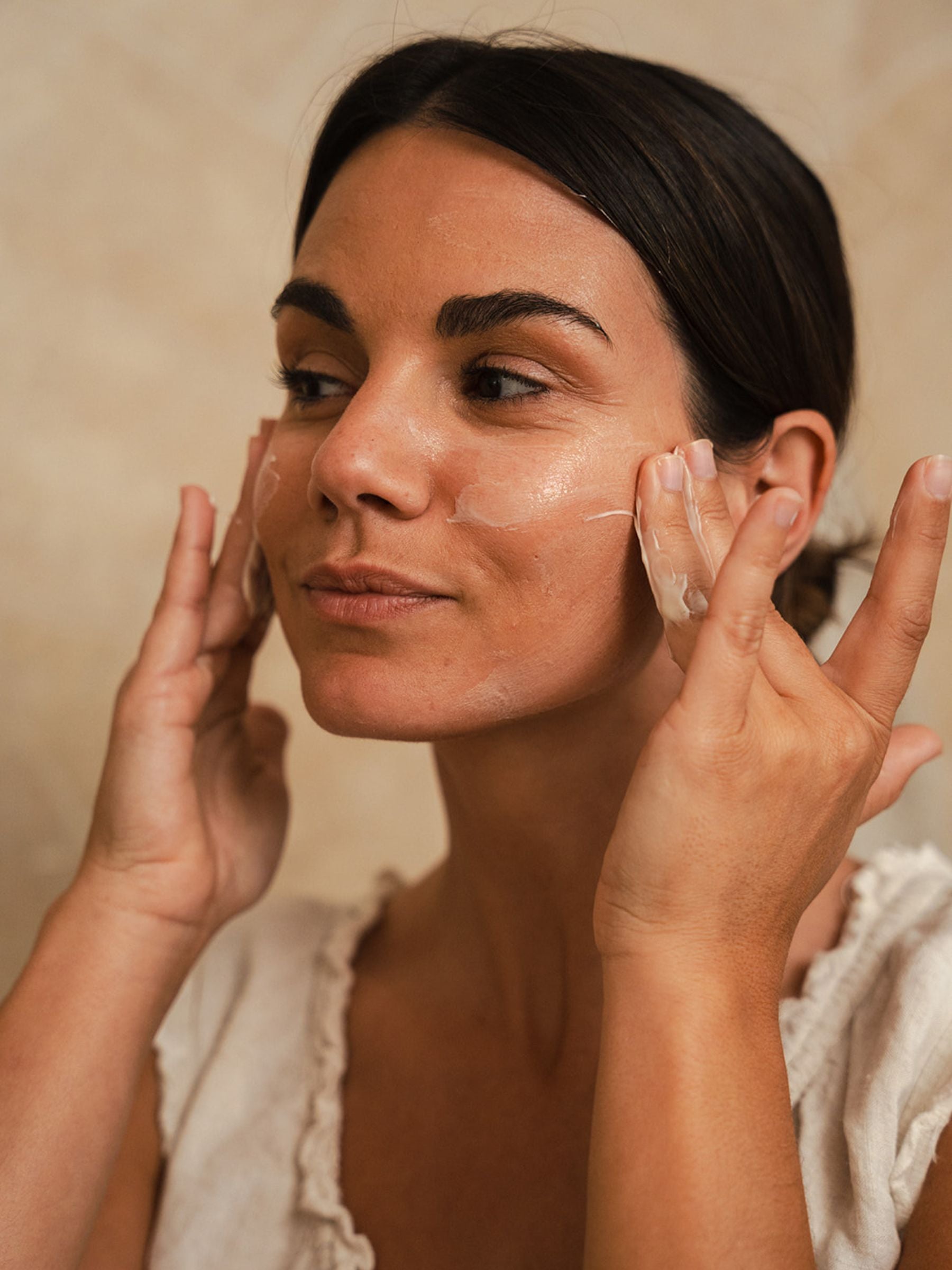 Woman gently massaging Organicspa Day Moisture facial moisturiser into her cheeks, showing hydrated, glowing skin.