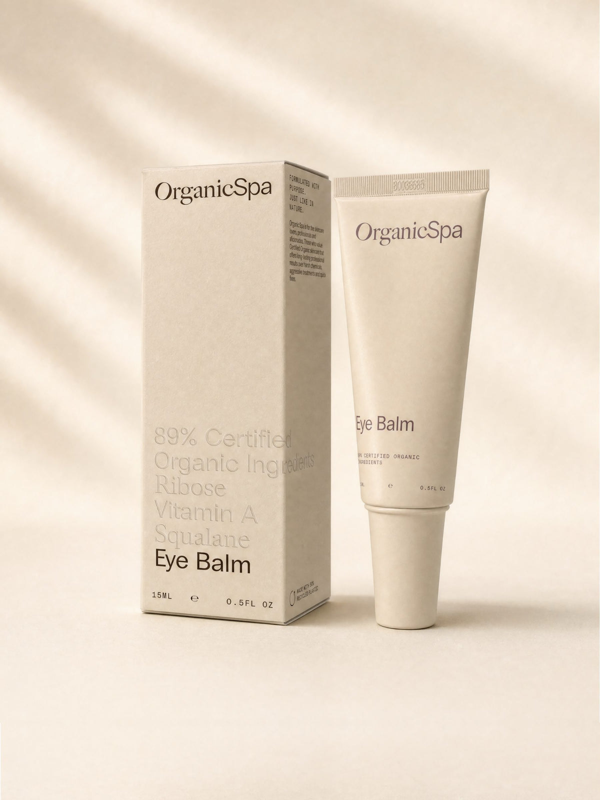 OrganicSpa Eye Balm, a sand-coloured 15ml tube standing beside its matching carton. The carton reads 89% Certified Organic Ingredients, Ribose, Vitamin A, Squalane, and made with 50% recycled plastic.