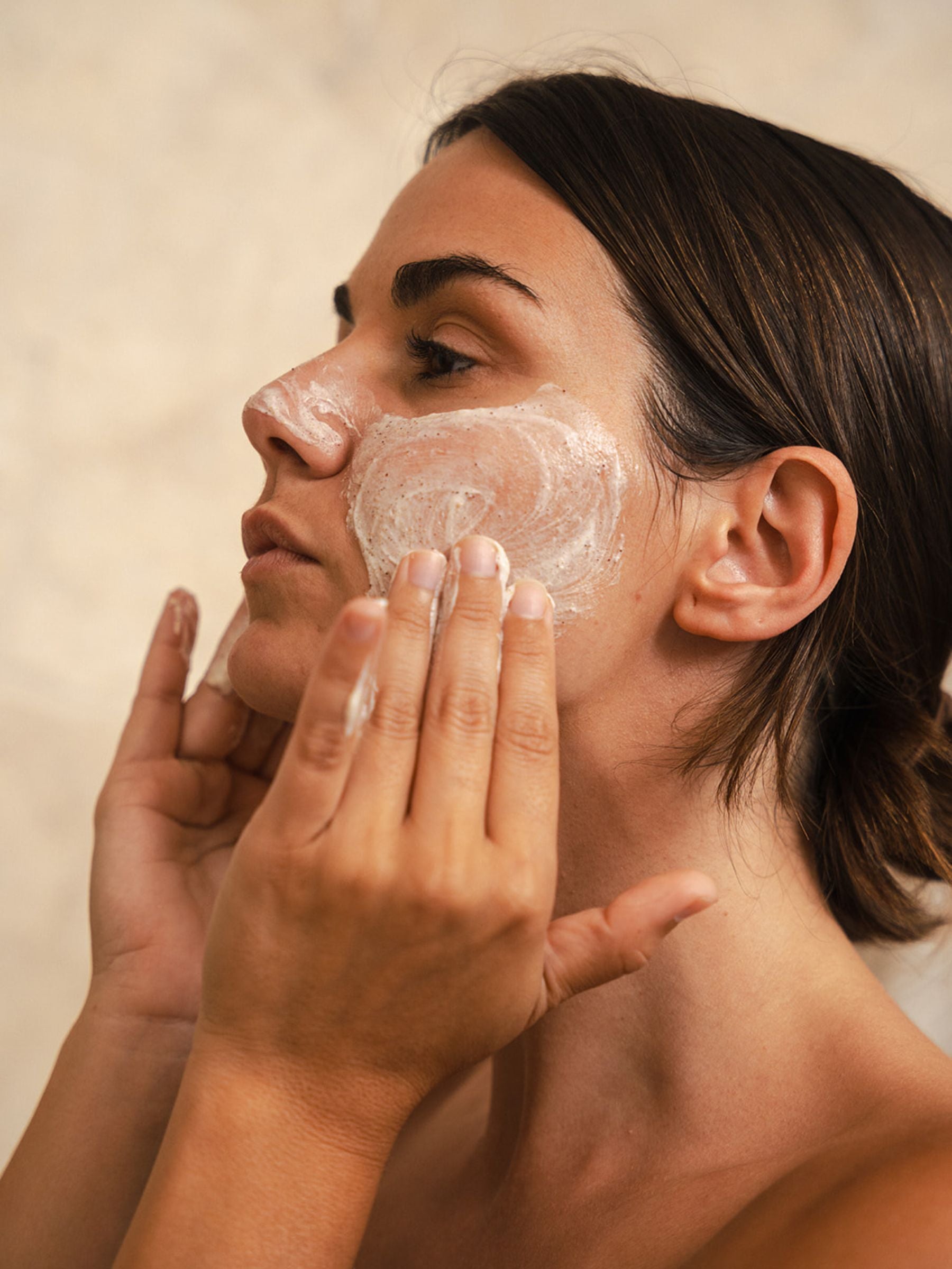 Woman gently massaging Organicspa Face Exfoliant onto her cheek, showing the creamy certified organic scrub texture on the skin.