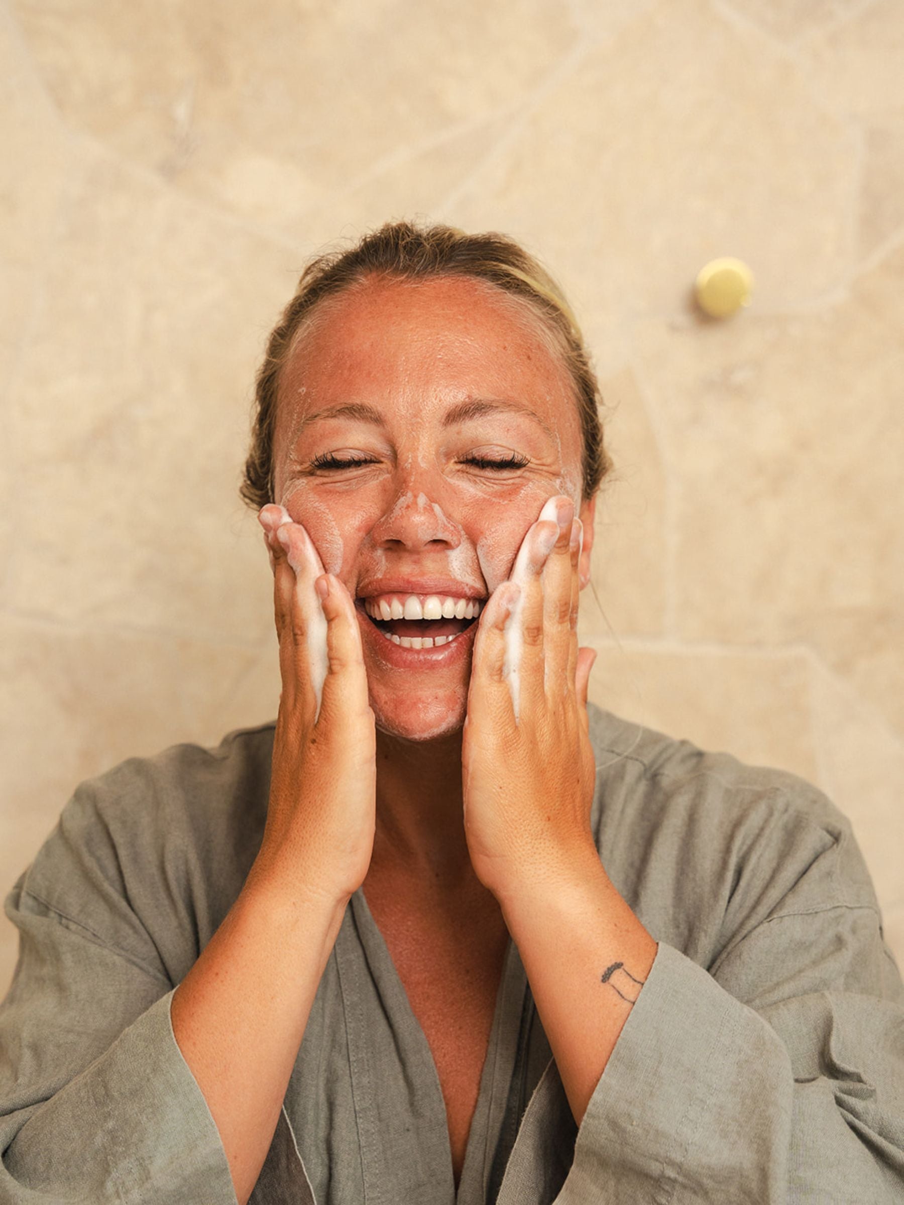 Woman smiling as she massages Organicspa Foam Cleanser over her face, creating a gentle foam during her cleansing ritual.