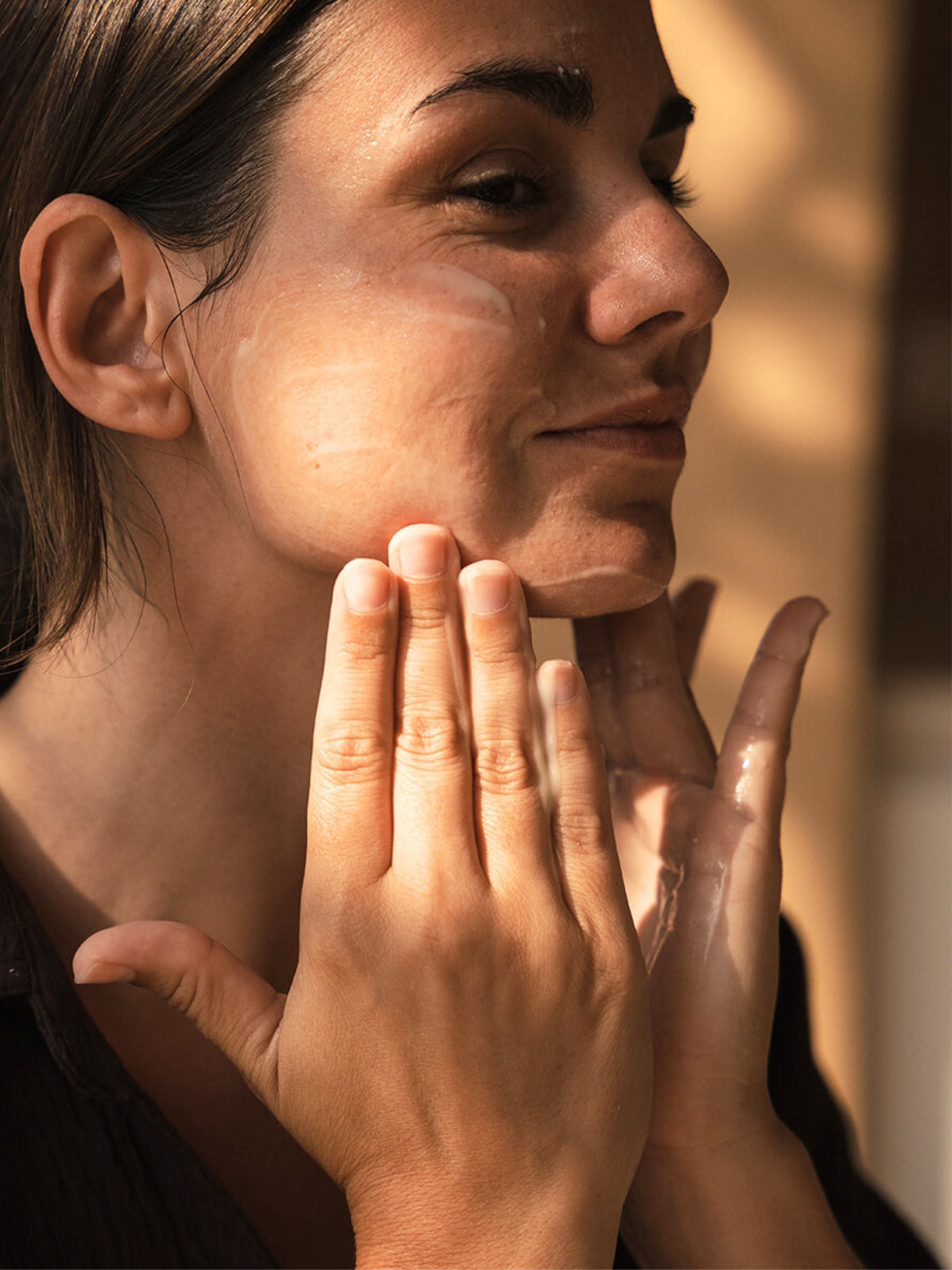 Woman gently applying Organicspa Gel Mask to her face, bathed in warm light with a fresh, dewy complexion.