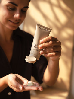 Woman squeezing Organicspa Gel Mask into her palm, showing the cooling gel texture in soft, natural light.
