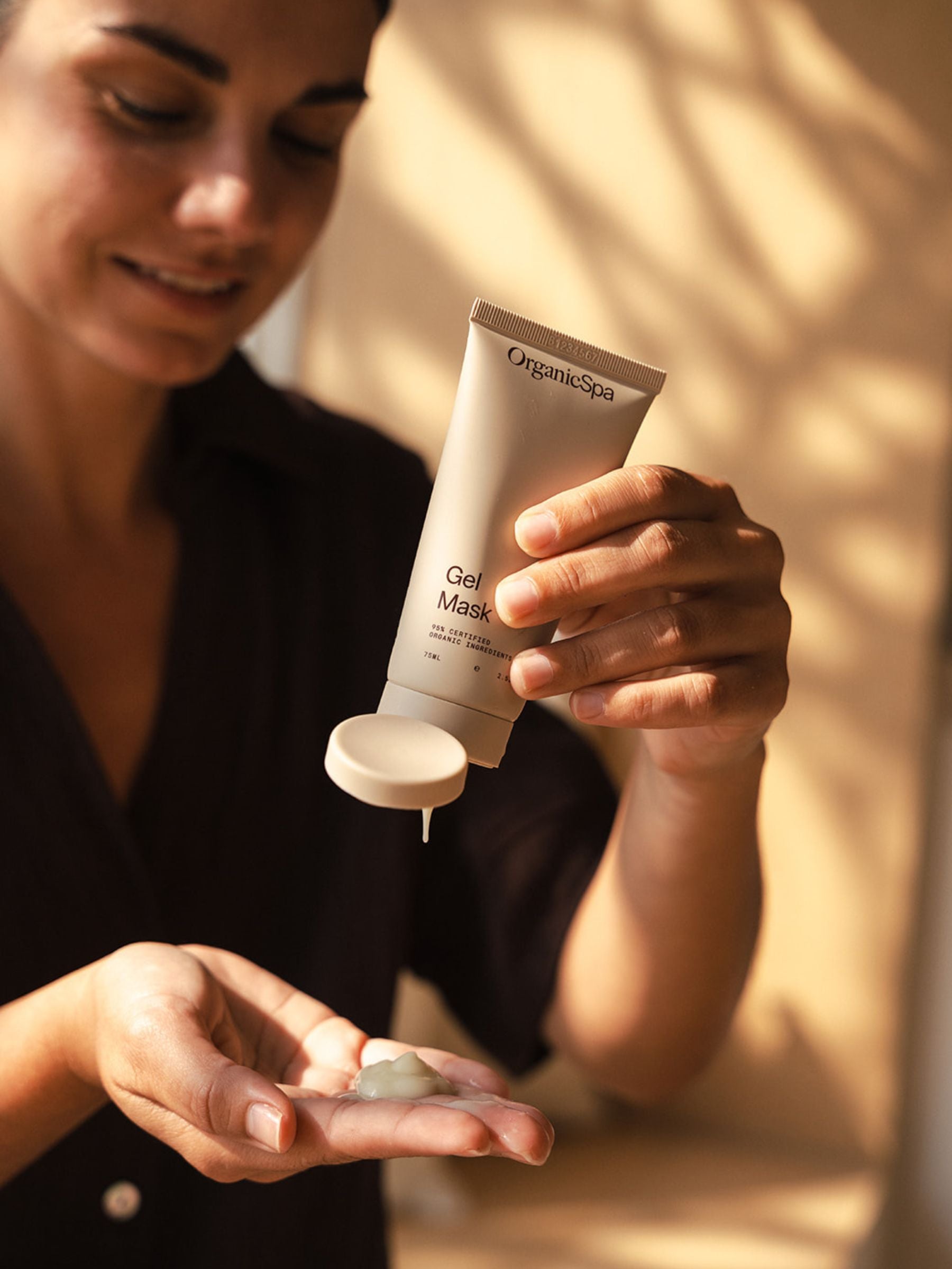 Woman squeezing Organicspa Gel Mask into her palm, showing the cooling gel texture in soft, natural light.