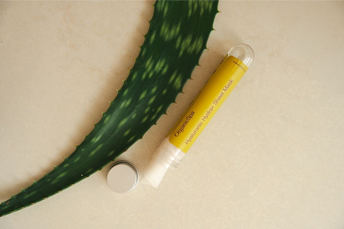Flatlay of an OrganicSpa Hyaluronic Hydra+ Sheet Mask vial alongside a fresh aloe vera leaf, emphasizing the potent botanical actives in our vegan skincare range.