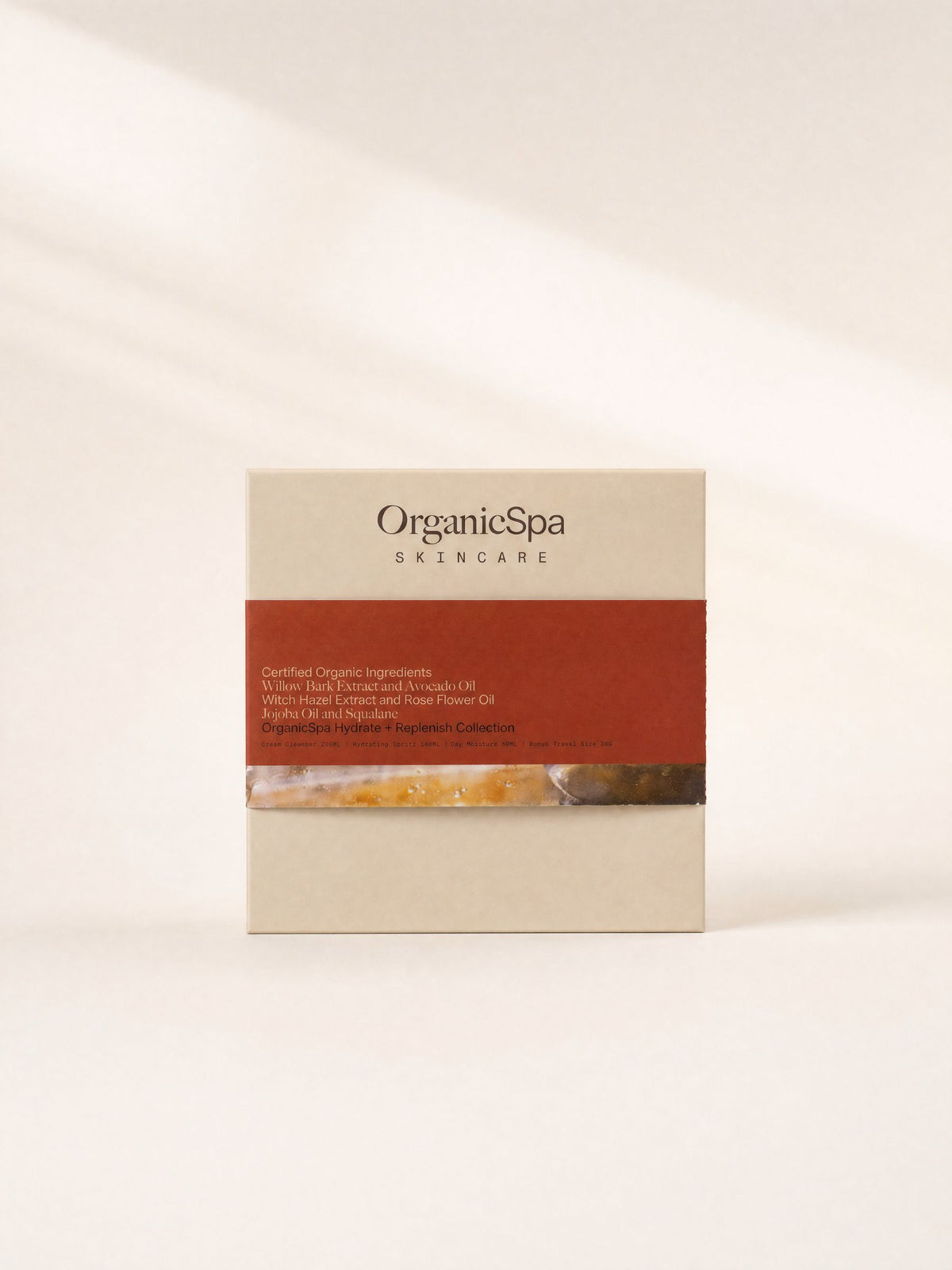 OrganicSpa Hydrate + Replenish Collection in a cream gift box with a rust red band. The band reads Certified Organic Ingredients, Willow Bark Extract and Avocado Oil, Witch Hazel Extract and Rose Flower Oil, Jojoba Oil and Squalane, and lists the contents as Cream Cleanser 200ml, Hydrating Spritz 140ml, Day Moisture 50ml and a bonus travel size 30g.