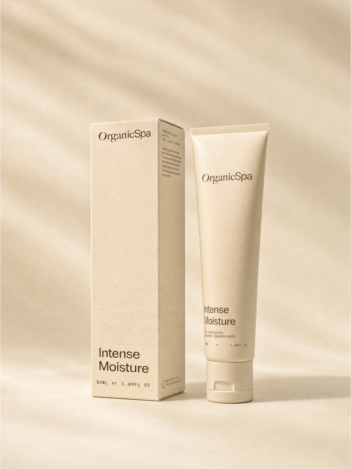 OrganicSpa Intense Moisture, a sand-coloured 50ml tube standing beside its matching carton. The carton reads 87% Certified Organic Ingredients, Cocoa Seed Butter, Carrot Seed Oil, Hyaluronic Acid, and made with 50% recycled plastic.