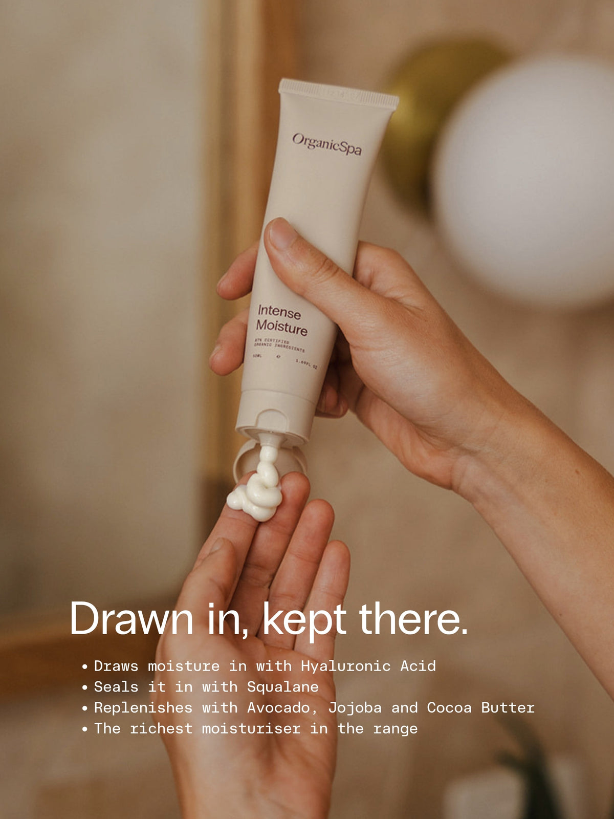 OrganicSpa Intense Moisture, a sand-coloured 50ml tube dispensing white cream into an open hand. Drawn in, kept there. Draws moisture in with Hyaluronic Acid. Seals it in with Squalane. Replenishes with Avocado, Jojoba and Cocoa Butter. The richest moisturiser in the range.