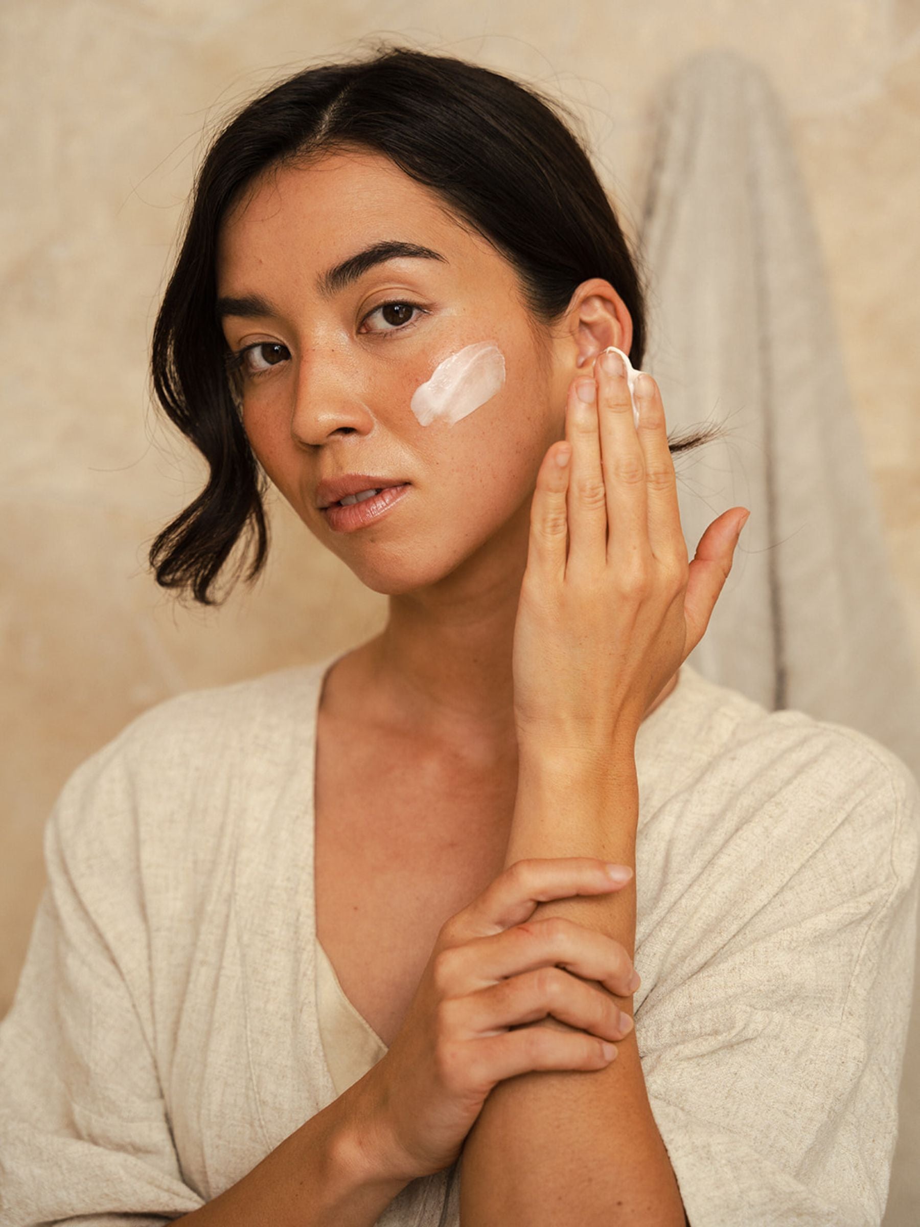 Woman applying Organicspa Intense Moisture cream to her cheek, showing the soft pink moisturiser on the skin.