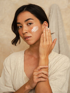 Woman applying Organicspa Intense Moisture cream to her cheek, showing the soft pink moisturiser on the skin.