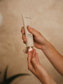 Hands squeezing Organicspa Intense Moisture from a tube onto fingertips, showing the rich cream texture.