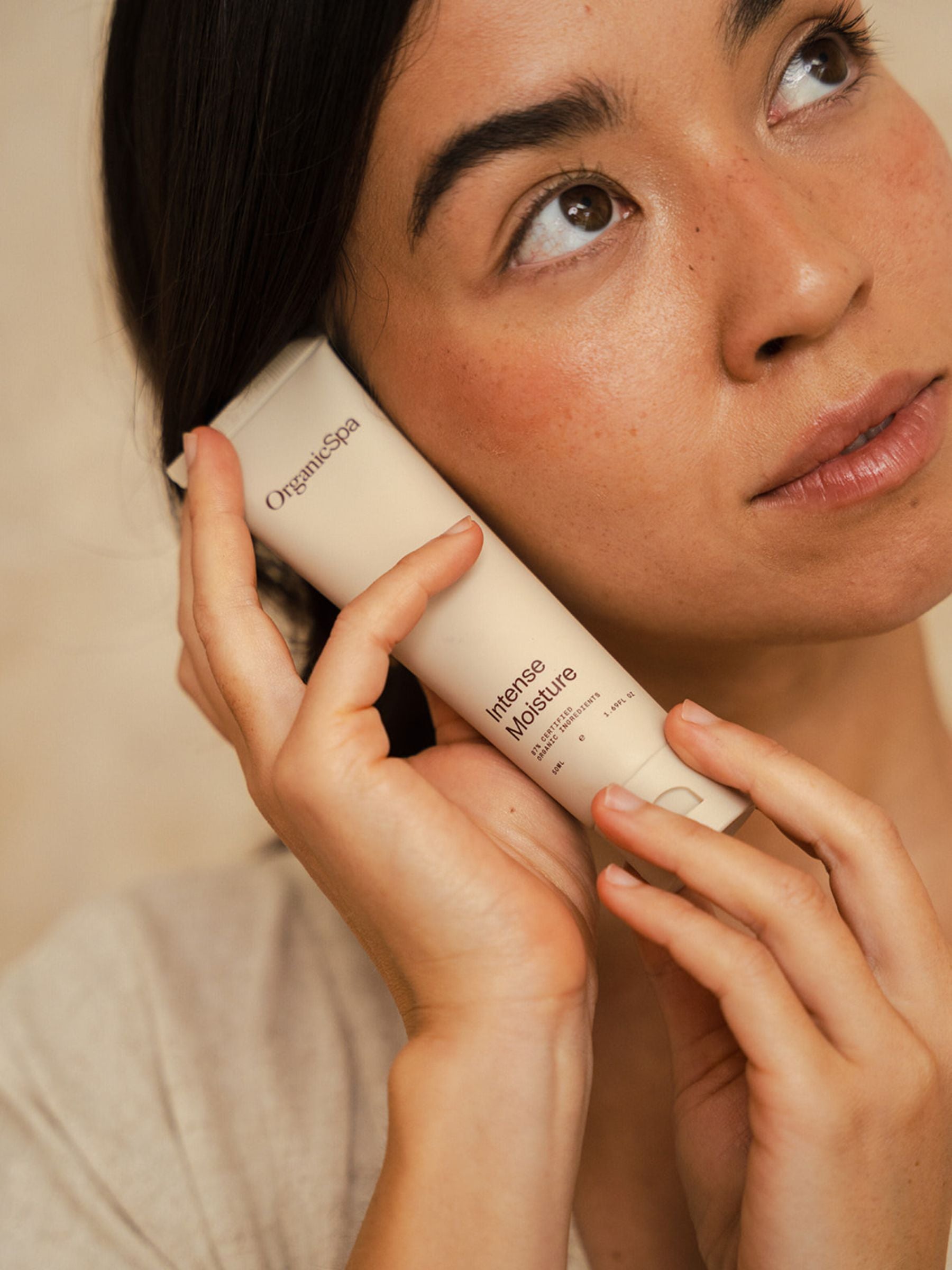 Woman holding a tube of Organicspa Intense Moisture against her cheek, highlighting the certified organic face moisturiser.