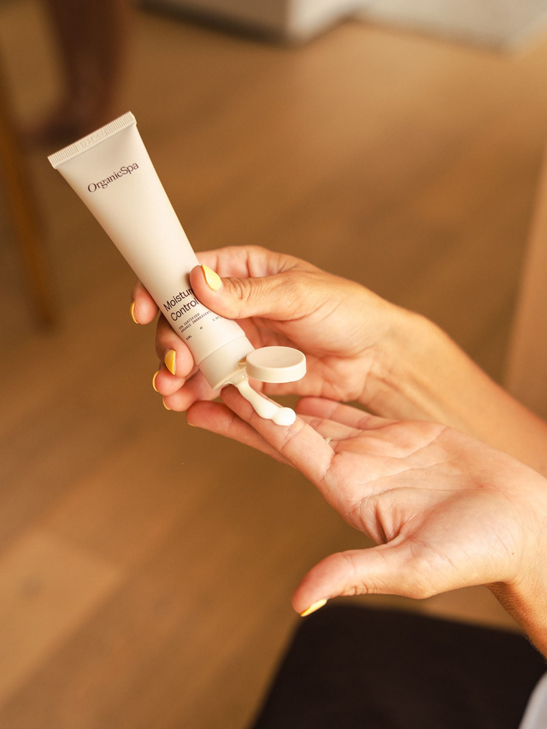 Hands dispensing Organicspa Moisture Control moisturiser from a beige tube onto fingertips, ready to apply to the skin.
