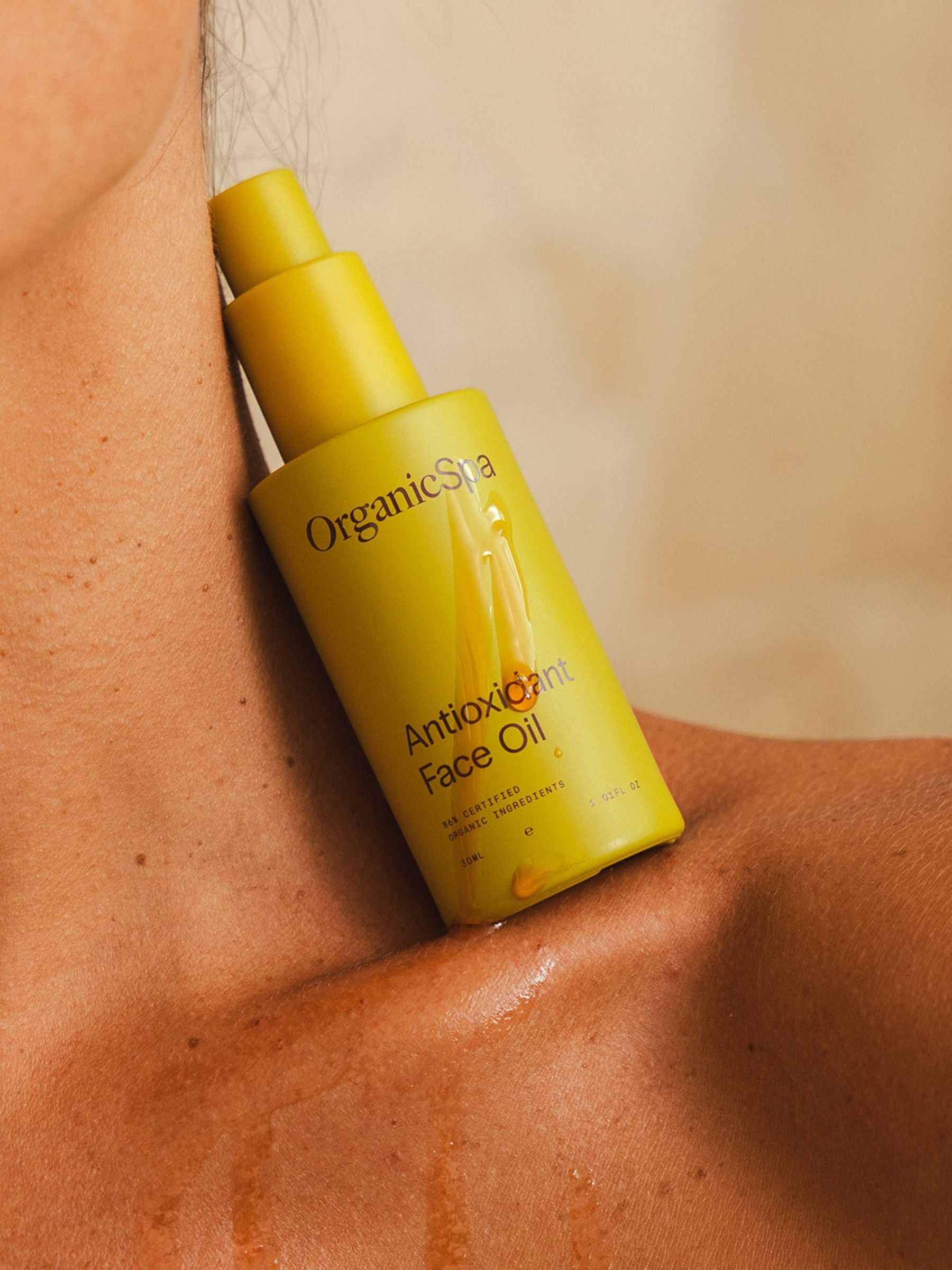 Bottle of Organicspa Organicsceuticals Antioxidant Face Oil resting on a woman’s collarbone with luminous oil on the skin, showcasing the certified organic facial oil in use.