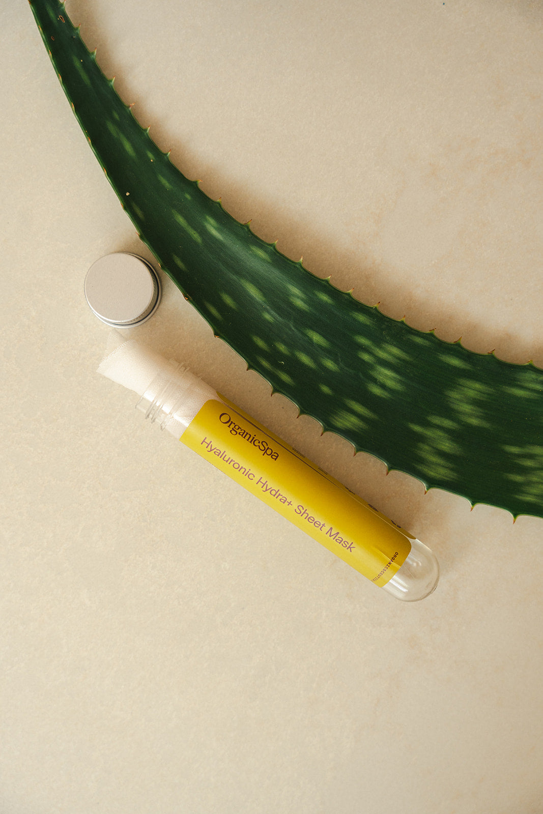 Tube of Organicspa Organicsceuticals Hyaluronic Hydra+ Sheet Mask Trio styled beside a fresh aloe leaf, highlighting hydrating certified organic skincare.