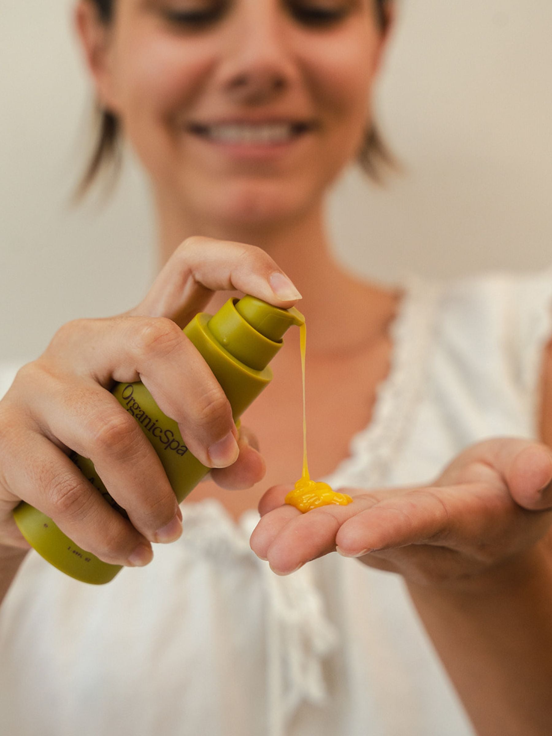 Close-up of a smiling woman dispensing bright orange Organicspa Organicsceuticals Vita-A+CE Complex serum into her palm.